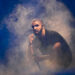 Drake performing on stage, surrounded by smoke, wearing a black shirt and holding a microphone.