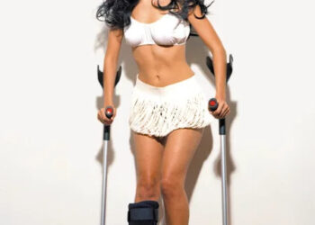 Woman in white outfit using crutches with a medical boot on her left leg.