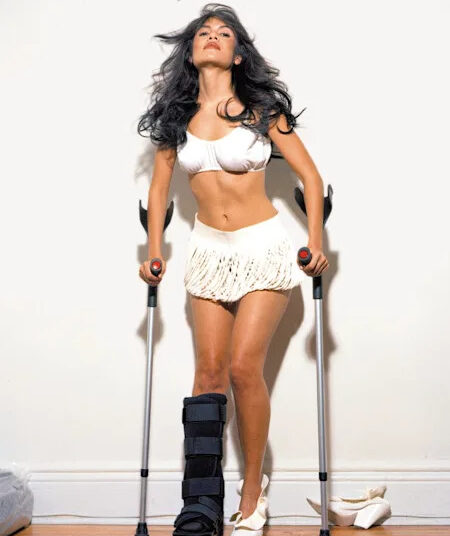 Woman in white outfit using crutches with a medical boot on her left leg.