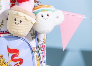Plushies from King Charles's Royal Collection Trust Shop including a pink strawberry cupcake toy keyring and a white cuddly cup keyring on a regal backpack