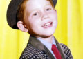 Ron Howard, US actor and director, wearing a grey hat and checked jacket, with a blue shirt and a red tie, in a studio portrait.