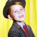 Ron Howard, US actor and director, wearing a grey hat and checked jacket, with a blue shirt and a red tie, in a studio portrait.