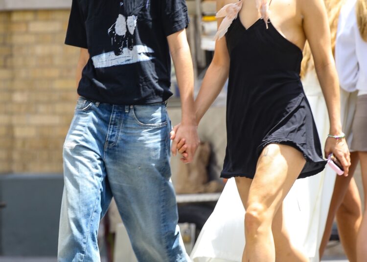 Rosalia wears a black mini dress with two feathers adorned to its straps and pointed-toe mules while holding hands with model Loli Bahia on a date in Manhattan
