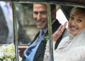 A woman is wearing a bridal dress sat in a car, smiling, and is sat next to a man in a wedding suit.