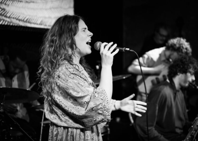 Ellyn Oliver singing on a stage with bandmates behind her.