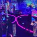 People playing glow-in-the-dark mini-golf with neon undersea-themed decor.