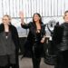 three women dressed in black wave to people behind and to the left of the camera