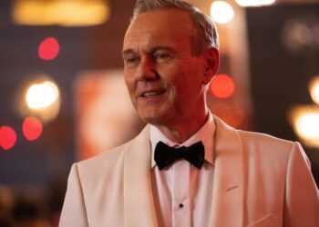 Anthony Stewart Head in a light-colored tuxedo and black bow tie, smiling.