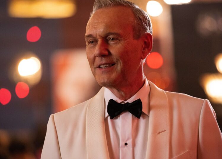 Anthony Stewart Head in a light-colored tuxedo and black bow tie, smiling.