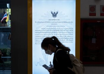 A woman wearing a mask walks past a video screen showing an official statement.