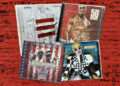 Four album covers on a red brick background: Jay-Z's "The Blueprint 3," 50 Cent's "Get Rich or Die Tryin'," The Diplomats' "Diplomatic Immunity," and Cardi B's "Invasion of Privacy." The albums feature some of the greatest New York City rap songs of all time.