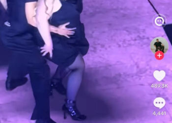 Dancers perform on stage during Ariana Grande's tour with one dancer in a dress with a mask on and others in black outfits