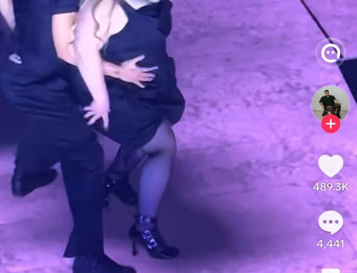 Dancers perform on stage during Ariana Grande's tour with one dancer in a dress with a mask on and others in black outfits