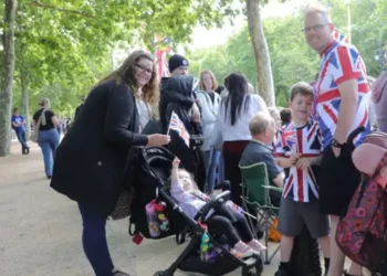 TIm and his children, one in a push chair, wear union shirts and stand near the barricade to watch the parade.