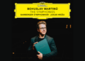 A man wearing glasses and a black shirt holds a large green book, standing under a bright Deutsche Grammophon label with Bohuslav Martinůs The Symphonies album information.