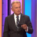 Pat Sajak reading a note card on Wheel of Fortune.