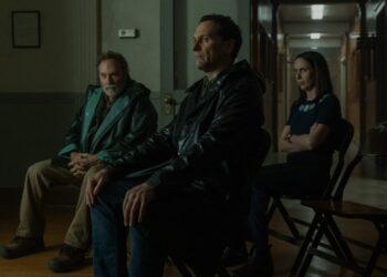 Three people sitting in a dimly lit room, one looking forward, one gazing sideways, and the other with arms crossed.