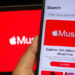 Apple Music displayed on smartphone with tablet with Apple Music logo in the background