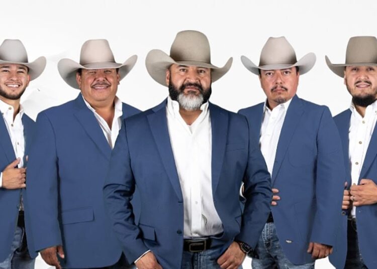 Five members of Cautivo Norteño wearing blue blazers and cowboy hats pose together in a studio portrait.