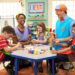 Three kids paint at a table beside a man and a woman.