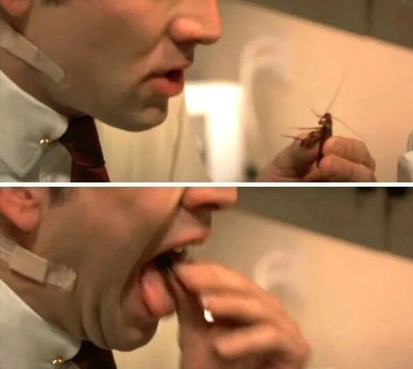 Nicolas Cage in a suit is holding a bug and preparing to eat it
