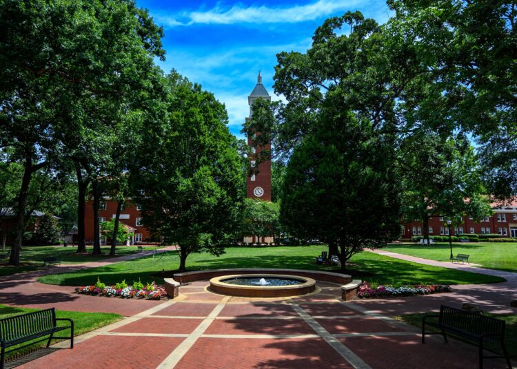 A picture of the Evans Clock Tower on the Queens University campus with a brick plaza in the foreground and trees surrounding the view.