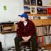 Image may contain Finn Wolfhard Baseball Cap Cap Clothing Hat Person Sitting Pants Teen Face Head and Photography