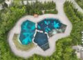 A drone view of three large outdoor pools, surrounded by concrete and green trees. Dolphins or beluga whales can be seen swimming in the pools.
