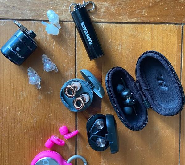 Five pairs of various earplugs and cases laid on a wood table.