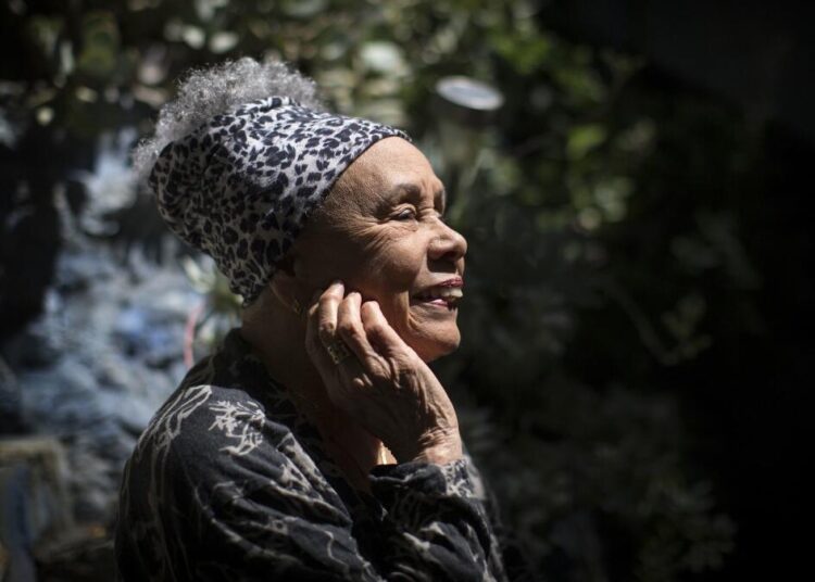 Betye Saar seen in profile and smiling ebulliently as the sun hits her face.