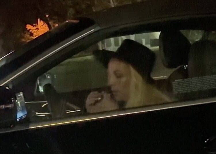 Britney Spears in the driver's seat of a black convertible BMW at night.