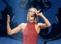 Celine Dion singing into a microphone, wearing a red sequined sleeveless, high-neck dress