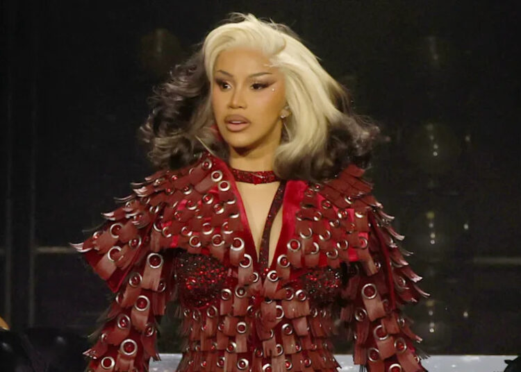 Cardi B performing in a striking red outfit with silver accents and two-tone hair on stage.