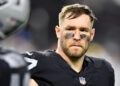 A football player in a black uniform with eye black, looking serious during a game.
