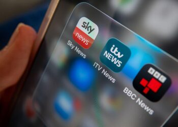 BATH, UNITED KINGDOM - NOVEMBER 08: A photo illustration of a man holding a phone, that shows ITV and Sky and BBC news apps on his phone screen on November 8, 2025 in Bath, England. ITV has said it is in the early stage of discussions to sell its broadcasting business to Sky in a move that could reshape the UK&amp;apos;s linear television landscape as it continues to come under increased competition from streaming services. (Photo by Anna Barclay/Getty Images)