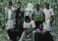 A group of nine people wearing green and white sportswear, standing and sitting against a matching abstract background.