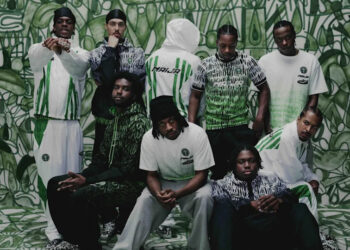 A group of nine people wearing green and white sportswear, standing and sitting against a matching abstract background.