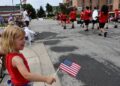 Aubrey Jannene waves a flag at a passing march band. Photo by Jeramey Jannene.