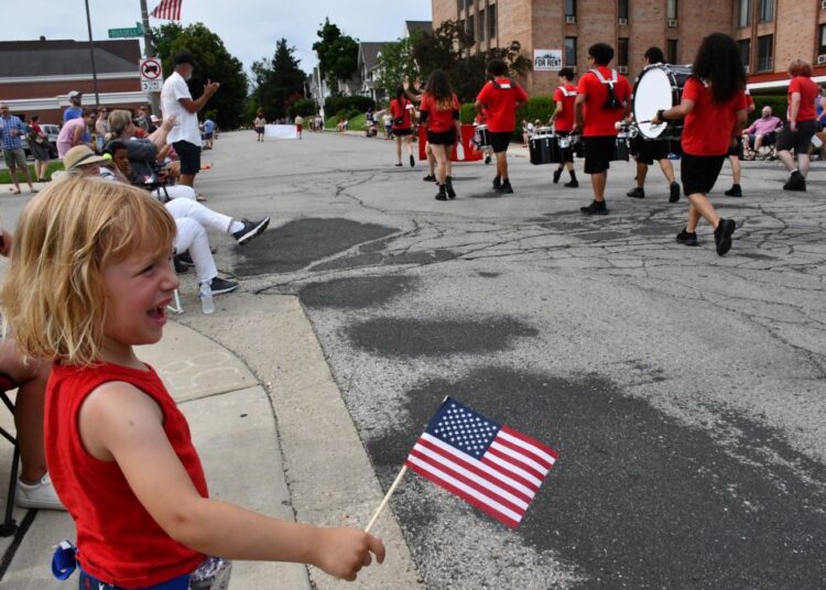 Aubrey Jannene waves a flag at a passing march band. Photo by Jeramey Jannene.