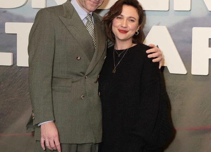 Rafe Spall and Esther Smith smiling, posing for a photo in front of a large 'UNDER SALT MARSH' sign.