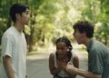 Three young people arguing on a forest road, with one person shouting and others showing emotional distress.