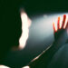 A hand reaching towards a bright light in a dark setting, with the figure's silhouette partially visible.