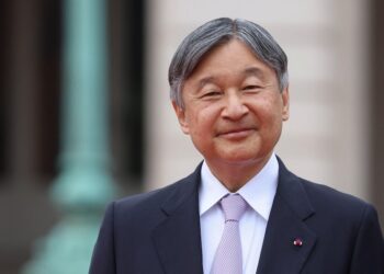 An older Japanese man in a neat suit smiles warmly at the camera.