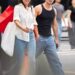 A woman in a white shirt and a man in a black tank top walking together on a city street, carrying shopping bags.