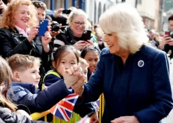 Queen Camilla in a blue coat shakes the hand of a schoolchild during her visit to the Isle of Man
