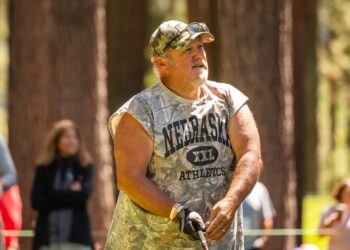 Larry the Cable Guy wearing a camouflage shirt and hat, playing golf.