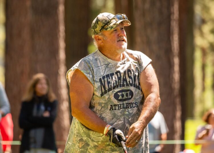 Larry the Cable Guy wearing a camouflage shirt and hat, playing golf.