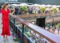 The Princess of Wales, in a red dress, waves to the crowd at Wimbledon as she walks across a bridge