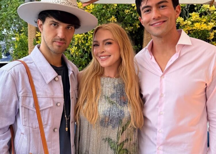 Three people celebrating a birthday outdoors, with festive attire and a decorative backdrop.