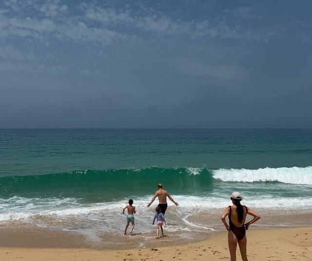 Family enjoying a beach day, with two children running toward the waves and an adult observing from the shore.